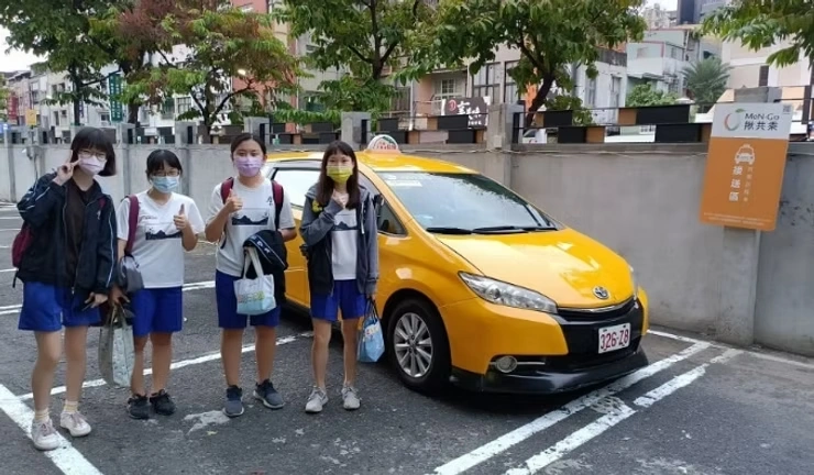 MeN Go 共乘案例照片：數名穿制服的人站在黃色計程車旁，背景為校園周邊街道。