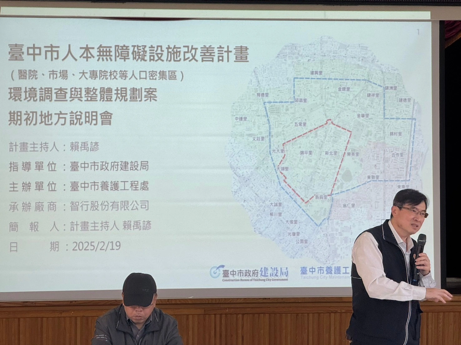 一中人本環境改善地方說明會照片，講者手持麥克風，後方投影人本無障礙設施改善計畫與道路位置圖。